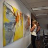 Two women admire large abstract canvases hung on clear perlon wires from an ArtiTeq Click Rail Pro picture rail in an office