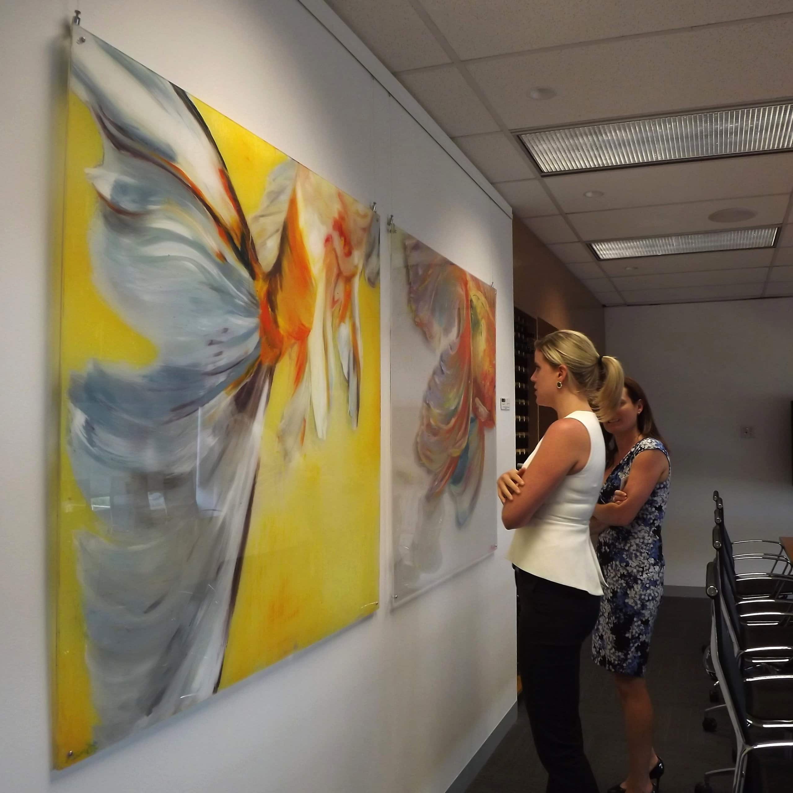 Two women admire large abstract canvases hung on clear perlon wires from an ArtiTeq Click Rail Pro picture rail in an office