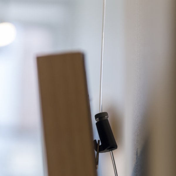 Transparent 1 mm Perlon Twister cable with black Micro Grip hook supporting a timber picture frame, showing minimal forward tilt against the wall.”