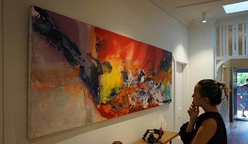 Woman admiring a vibrant abstract painting hung using Artiteq Click Rail Pro from Hang Logic.
