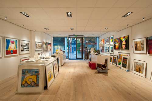 Art gallery filled with artworks, some hanged on railings against the wall , some lying against the wall and tables.