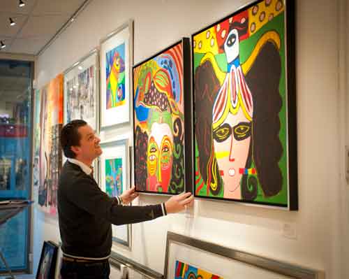 Man adjusting framed artwork on Artiteq Combi Rail Pro Light picture rail system with integrated lighting at Hang Logic.