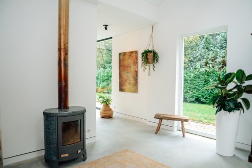 Modern living space with wood stove, Artiteq Shadowline picture rail from Hang Logic, hanging artwork and potted plants.