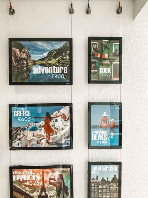 Travel posters displayed on a wall using a cable hanging system, showcasing various travel destinations.