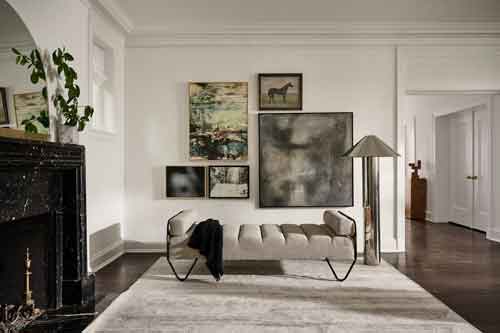 Living Room with Gallery Wall and Beige Bench Living room with a gallery wall of various artworks, a beige bench, a large floor lamp, and a black marble fireplace.