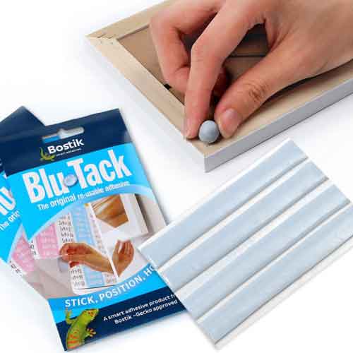 Blu-Tack product packaging with a close-up of a person applying it to the back of a frame for hanging.