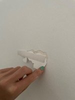 Hand peeling off adhesive from a wall, causing damage to the paint and plaster.