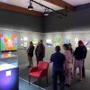 Visitors viewing colourful paintings lit from a wall‑mounted Combi Rail Pro Light picture hanging and lighting track