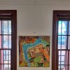 Textile map quilt hung on a clear loop cable attached to a white ArtiTeq picture rail between timber‑framed windows, supplied by Hang Logic.