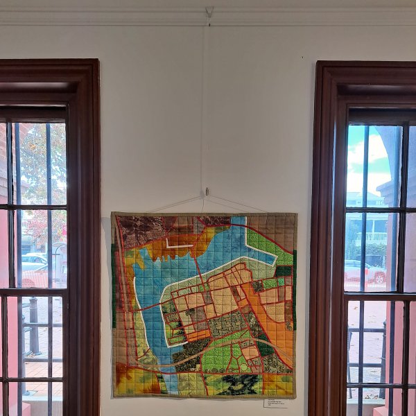Textile map quilt hung on a clear loop cable attached to a white ArtiTeq picture rail between timber‑framed windows, supplied by Hang Logic.