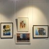 Four framed paintings hung on clear loop dropper wires attached to a white picture rail in a gallery setting, supplied by Hang Logic