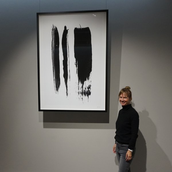 Woman standing beside large black and white print hung on clear wires from ArtiTeq Top Rail ceiling picture rail