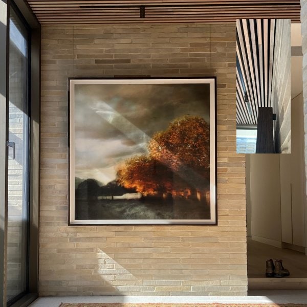 Large framed landscape hung on clear wires from ArtiTeq Top Rail concealed between timber ceiling slats above brick feature wall